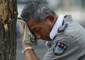 Agente de segurança usa um ventilador elétrico no pescoço e enxuga suor em dia quente em Pequim, na última segunda-feira, 3 de julho de 2023.