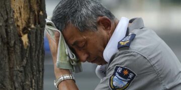 Agente de segurança usa um ventilador elétrico no pescoço e enxuga suor em dia quente em Pequim, na última segunda-feira, 3 de julho de 2023.