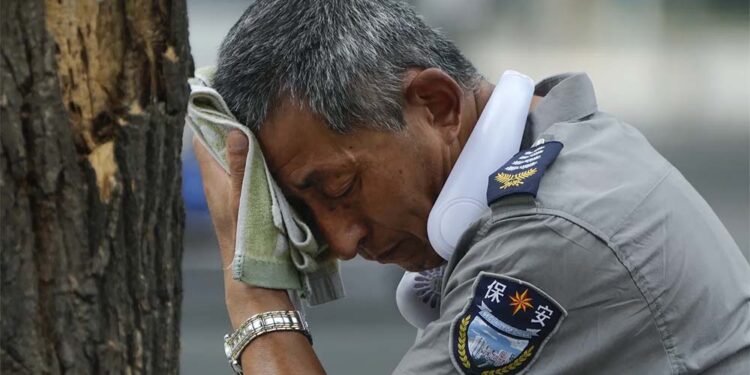 Agente de segurança usa um ventilador elétrico no pescoço e enxuga suor em dia quente em Pequim, na última segunda-feira, 3 de julho de 2023.