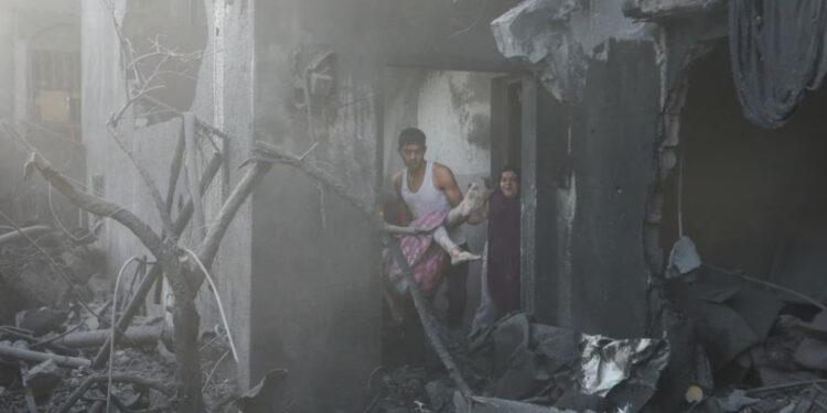 Um homem carrega uma menina palestina ferida no local dos ataques israelenses a uma casa, em Khan Younis, no sul da Faixa de Gaza.